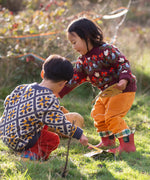 Children wearing Little Green Radicals organic cotton knitted jumpers. One has a folk birds design the other has a  tile pattern knit.
