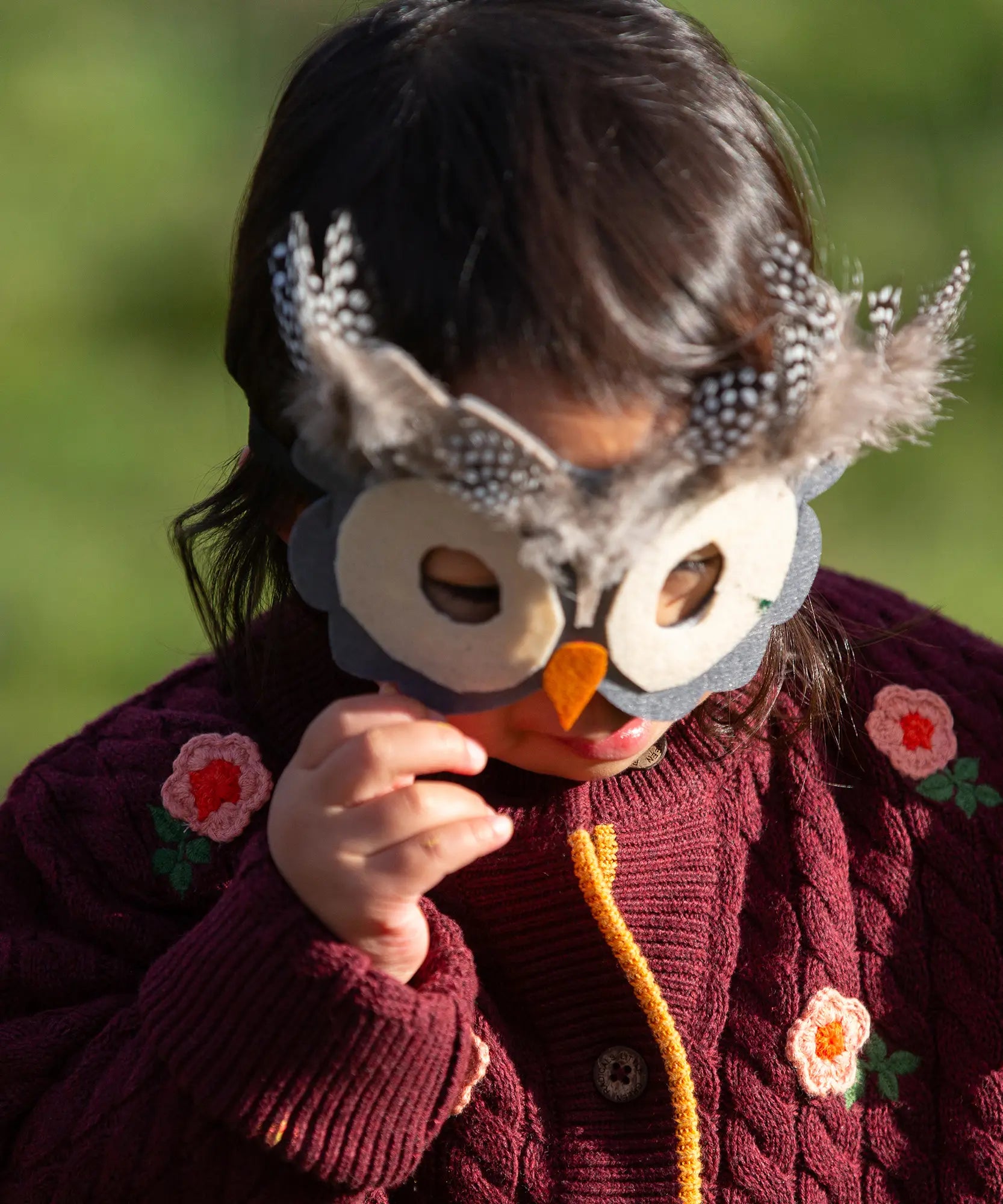 Close up of a child wearing the Little Green Radicals organic cotton snuggly knitted cardigan with a berry petal design. Dark purple cardigan with pink flowers details.