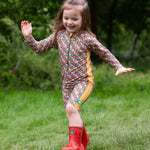 A child wearing the Little Green Radicals Vintage Flowers UPF 50+ Recycled Sunsafe Sunsuit with a pair of red wellington boots.