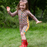 A child wearing the Little Green Radicals Vintage Flowers UPF 50+ Recycled Sunsafe Sunsuit with a pair of red wellington boots.