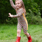 A child wearing the Little Green Radicals Vintage Flowers UPF 50+ Recycled Sunsafe Sunsuit with a pair of red wellington boots.