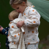 A child wearing the Little Green Radicals moon and sun classic pyjama set holding a matching Sherpa lined hooded blanket. A GOTS organic cotton pyjama set including a long sleeve shirt style top in light pink with prints of cute birds flying through stars the moon and sun also includes matching bottoms. These pyjamas are part of a wide range of organic cotton clothing for children available here at Babipur.