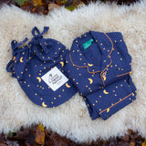 Little Green Radicals Dark Night  Organic Cotton Classic children's Pyjamas placed folded on a sheepskin rug. These navy blue traditional style pyjamas have a yellow moon and star print all over. These pyjamas are part of a wide range of organic cotton clothing for children available here at Babipur.