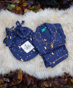 Little Green Radicals Dark Night  Organic Cotton Classic children's Pyjamas placed folded on a sheepskin rug. These navy blue traditional style pyjamas have a yellow moon and star print all over. These pyjamas are part of a wide range of organic cotton clothing for children available here at Babipur.