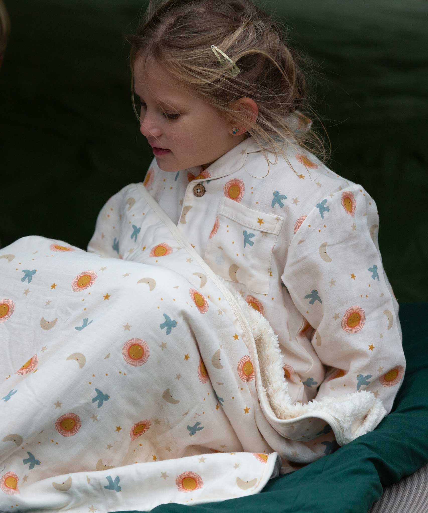 A child wearing the Little Green Radicals moon and sun classic pyjama set. A GOTS organic cotton pyjama set including a long sleeve shirt style top in light pink with prints of cute birds flying through stars the moon and sun also includes matching bottoms. These pyjamas are part of a wide range of organic cotton clothing for children available here at Babipur.