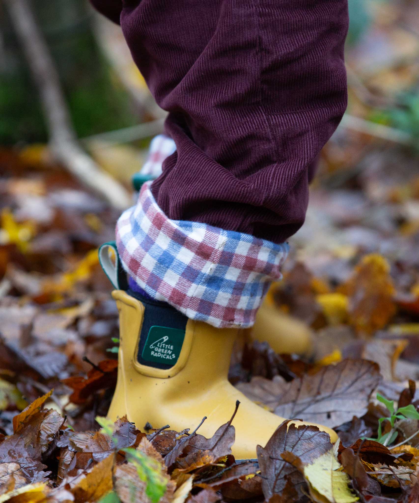 A close up of a child wearing the Little Green Radicals Chocolate brown Cord Lined Trousers with yellow gold wellington boots. These trousers are part of a wide range of organic cotton clothing for children available here at Babipur. 
