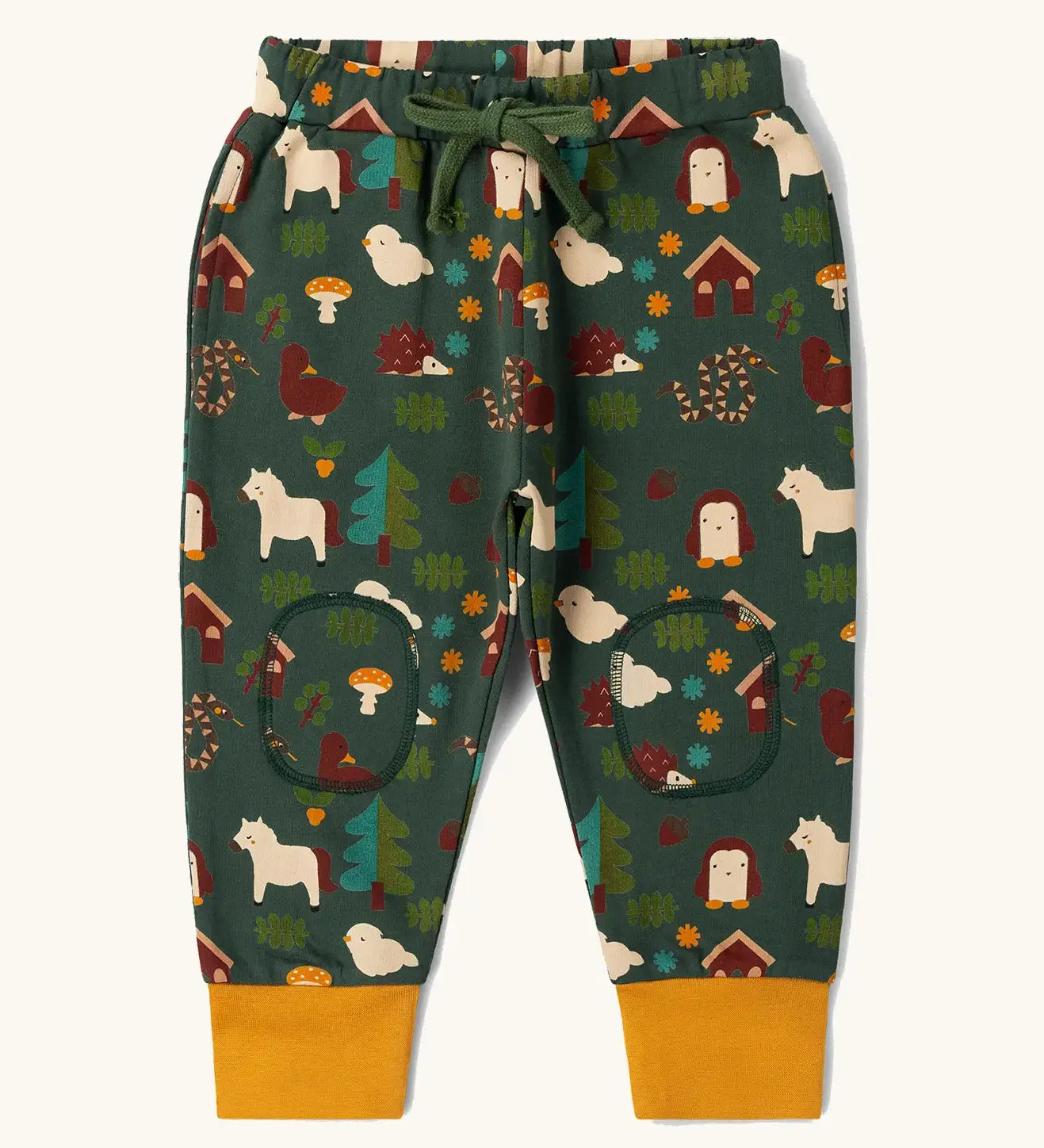  Little Green Radicals cosy organic cotton knee patch joggers with a woodland design print. Dark green joggers with a woodland print featuring animals, trees a hut.