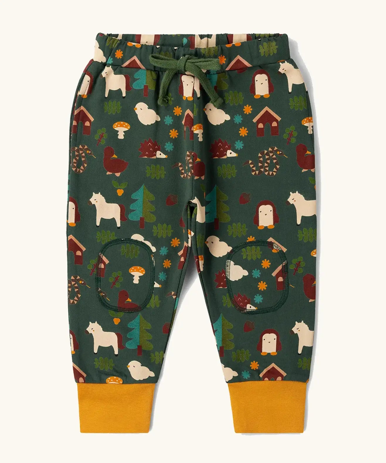  Little Green Radicals cosy organic cotton knee patch joggers with a woodland design print. Dark green joggers with a woodland print featuring animals, trees a hut.