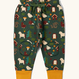  Little Green Radicals cosy organic cotton knee patch joggers with a woodland design print. Dark green joggers with a woodland print featuring animals, trees a hut.
