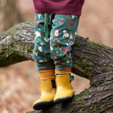 Child wearing the Little Green Radicals cosy organic cotton knee patch joggers with a woodland design print. Dark green joggers with a woodland print featuring animals, trees a hut.