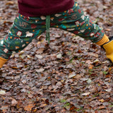 Child wearing the Little Green Radicals cosy organic cotton knee patch joggers with a woodland design print with yellow gold wellington boots.