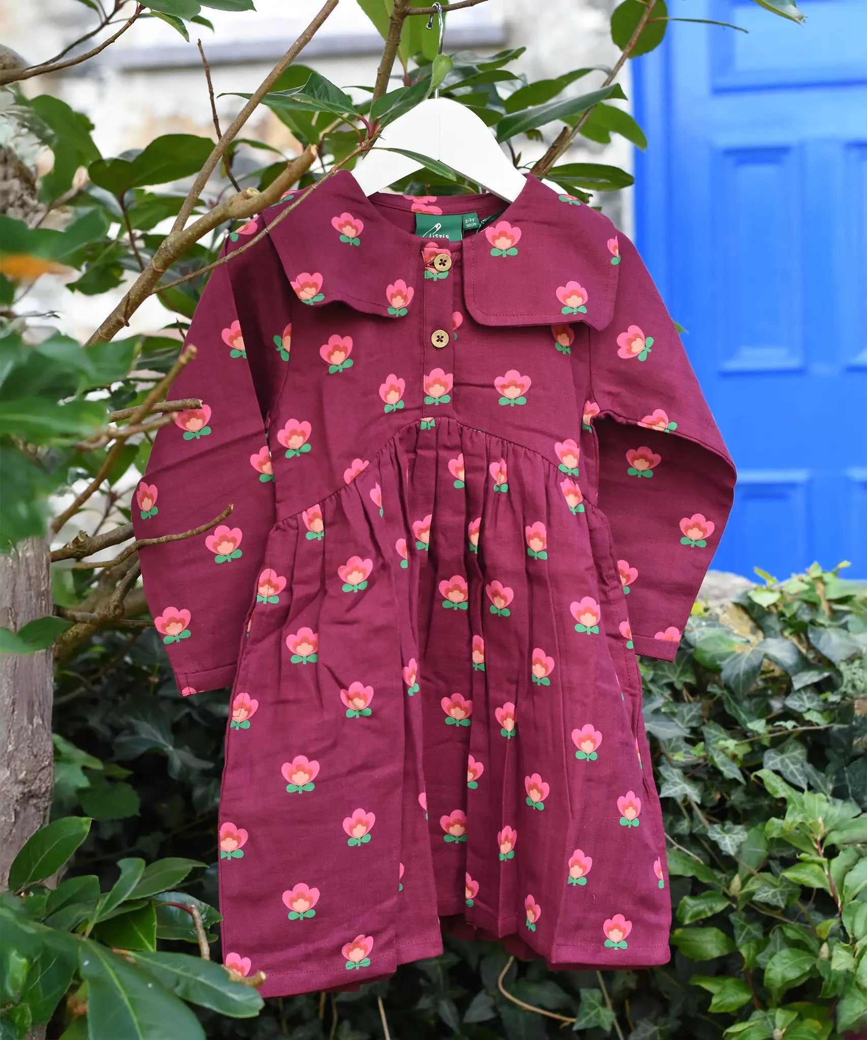 Little Green Radicals Pink Flowers Organic Cotton Sailor Dress hung up on a tree branch outdoors. 