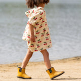 Child wearing the Little Green Radicals little cherries cream organic cotton kids hooded towel poncho.The poncho has a popper closure on the neck and a kangaroo pocket on the front. 