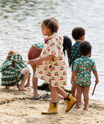 Side view of a child wearing the Little Green Radicals little cherries cream organic cotton kids hooded towel poncho.The poncho has a popper closure on the neck and a kangaroo pocket on the front. 