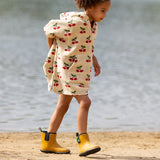 Child wearing the Little Green Radicals little cherries cream organic cotton kids hooded towel poncho with yellow wellington boots. The poncho has a popper closure on the neck and a kangaroo pocket on the front. 
