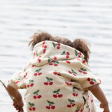 Back of a child wearing the Little Green Radicals little cherries cream organic cotton kids hooded towel poncho.The poncho has a popper closure on the neck and a kangaroo pocket on the front. 