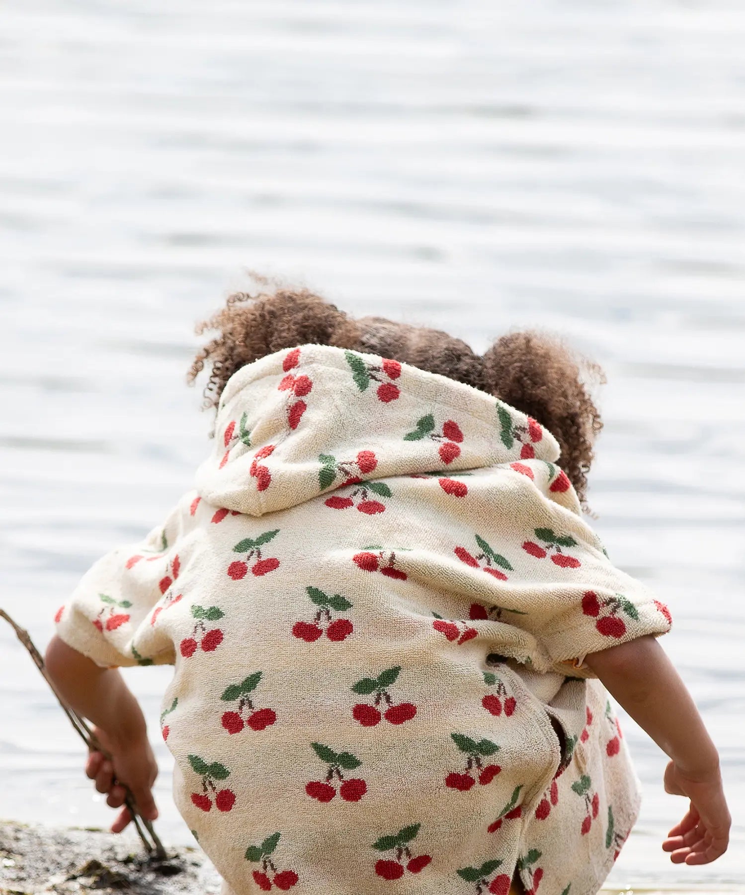 Back of a child wearing the Little Green Radicals little cherries cream organic cotton kids hooded towel poncho.The poncho has a popper closure on the neck and a kangaroo pocket on the front. 