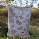 Child standing behind a Little Green Radicals cream folk tales knitted organic cotton baby blanket that they are holding up in front of them.