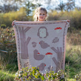 Child standing behind a Little Green Radicals cream folk tales knitted organic cotton baby blanket that they are holding up in front of them.