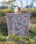 Child standing behind a Little Green Radicals cream folk tales knitted organic cotton baby blanket that they are holding up in front of them.