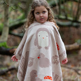 Child holding a Little Green Radicals cream folk tales knitted organic cotton baby blanket in front of them.