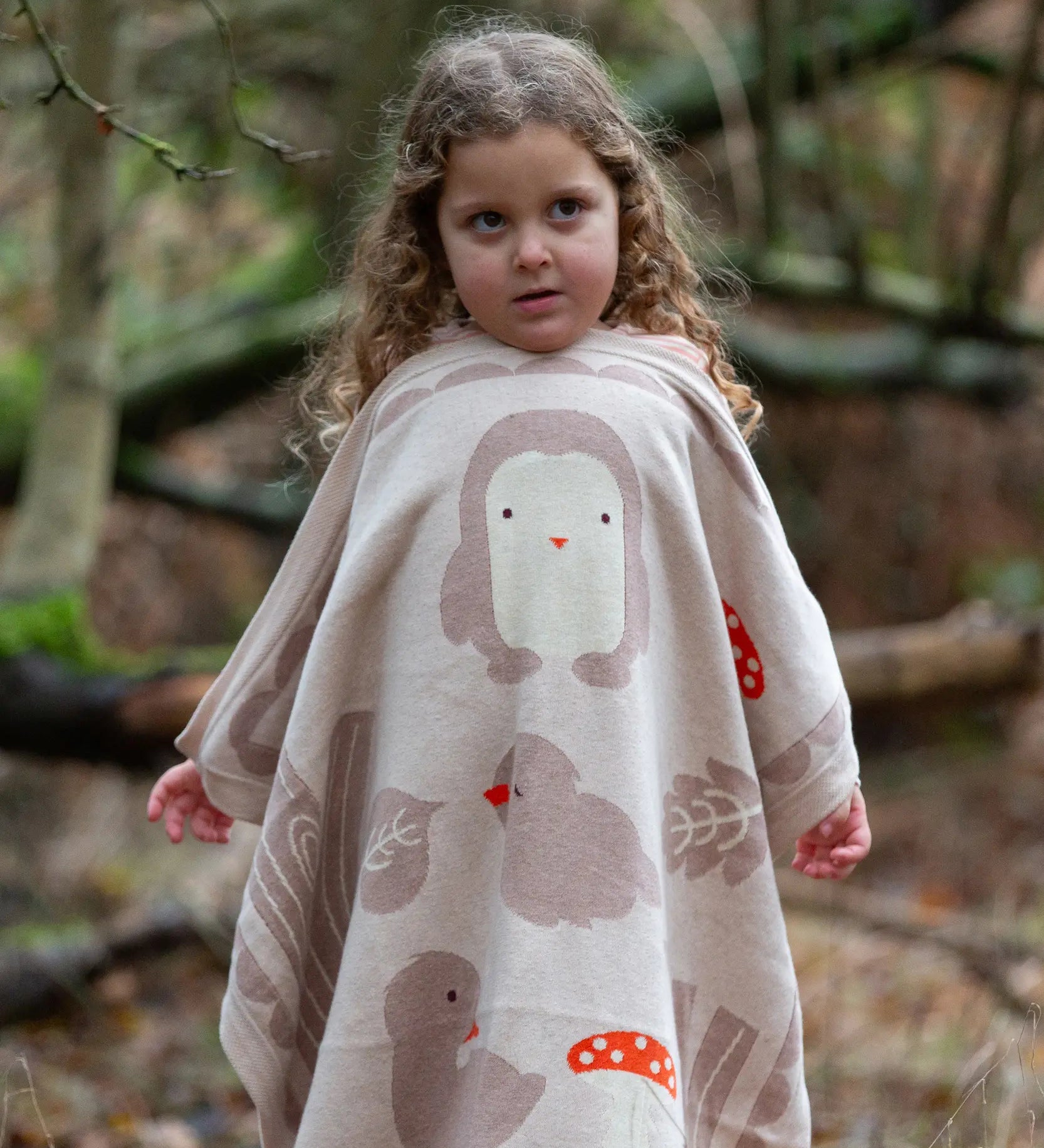 Child holding a Little Green Radicals cream folk tales knitted organic cotton baby blanket in front of them.