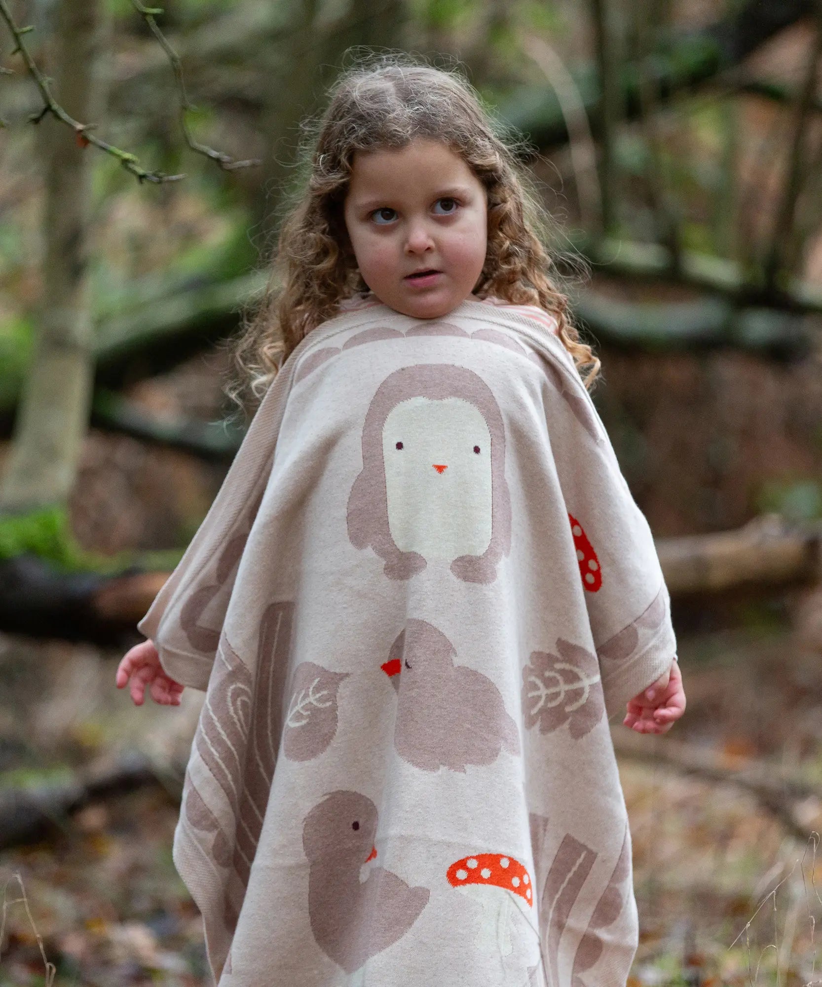 Child holding a Little Green Radicals cream folk tales knitted organic cotton baby blanket in front of them.