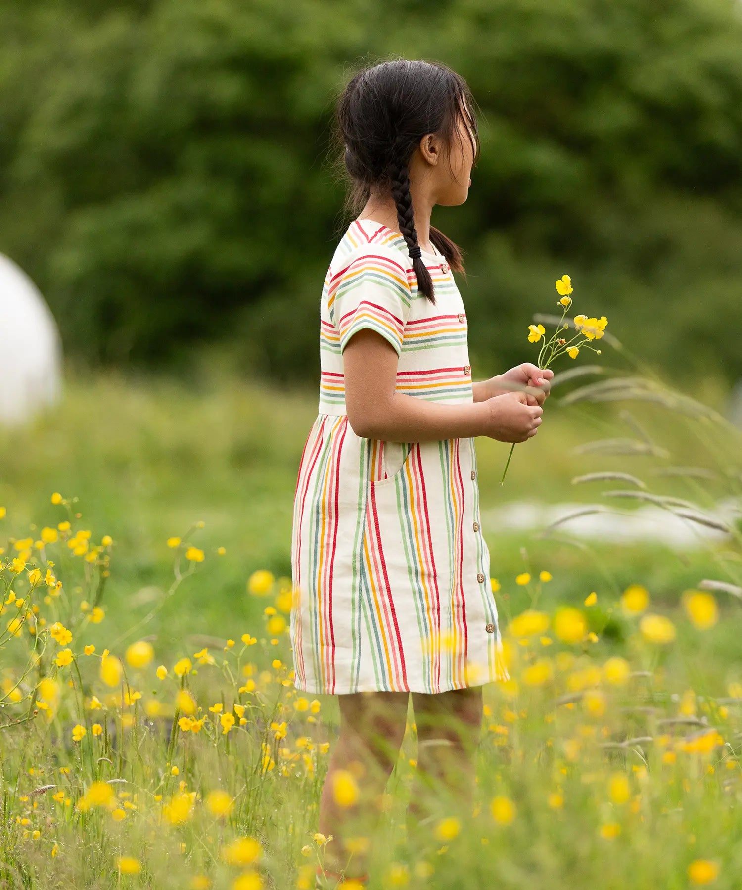 A child wearing the Little Green Radicals cream rainbow striped short sleeve button front dress.
