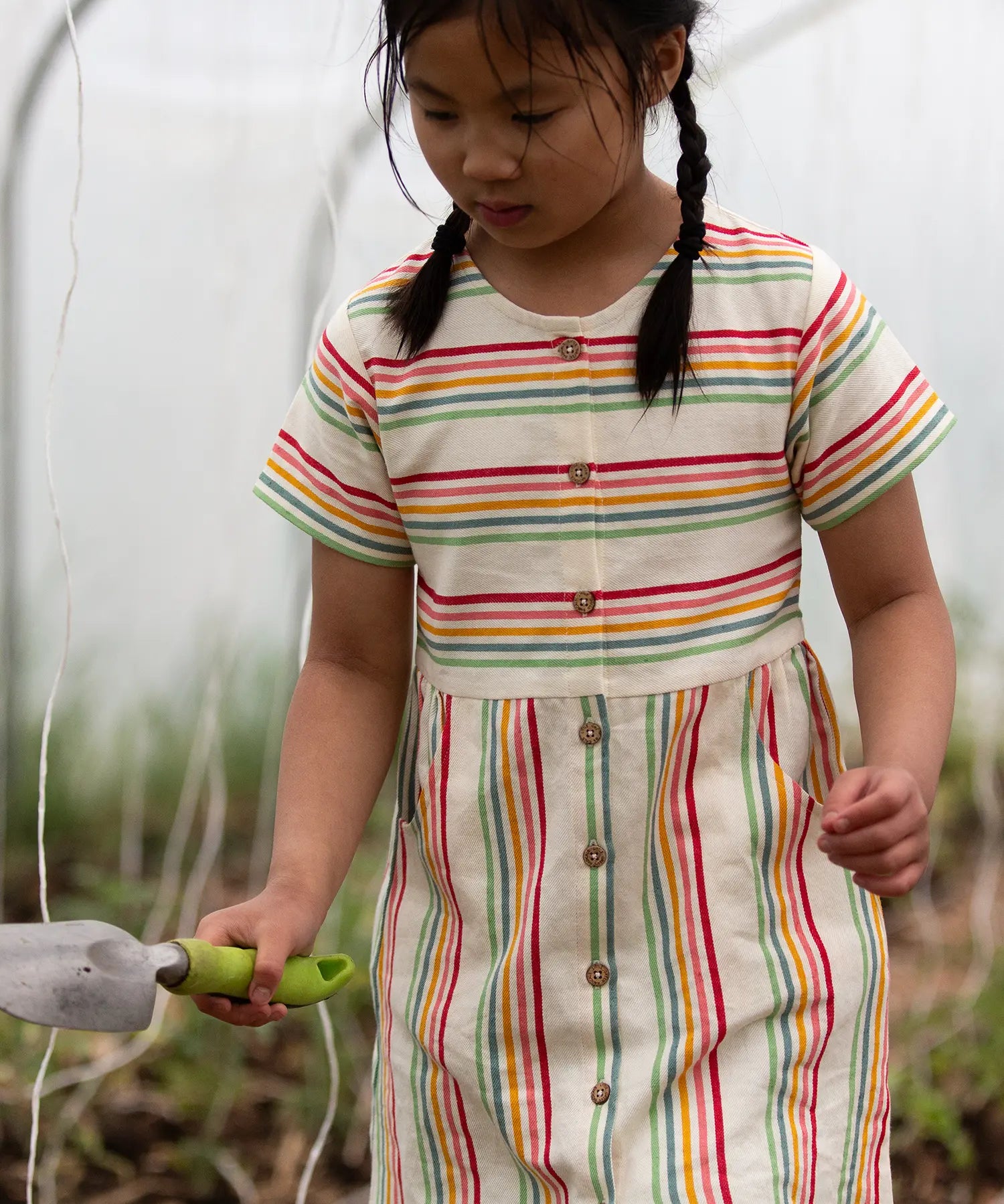 A child wearing the Little Green Radicals cream rainbow striped short sleeve button front dress.