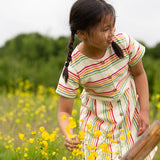 A child wearing the Little Green Radicals cream rainbow striped short sleeve button front dress.