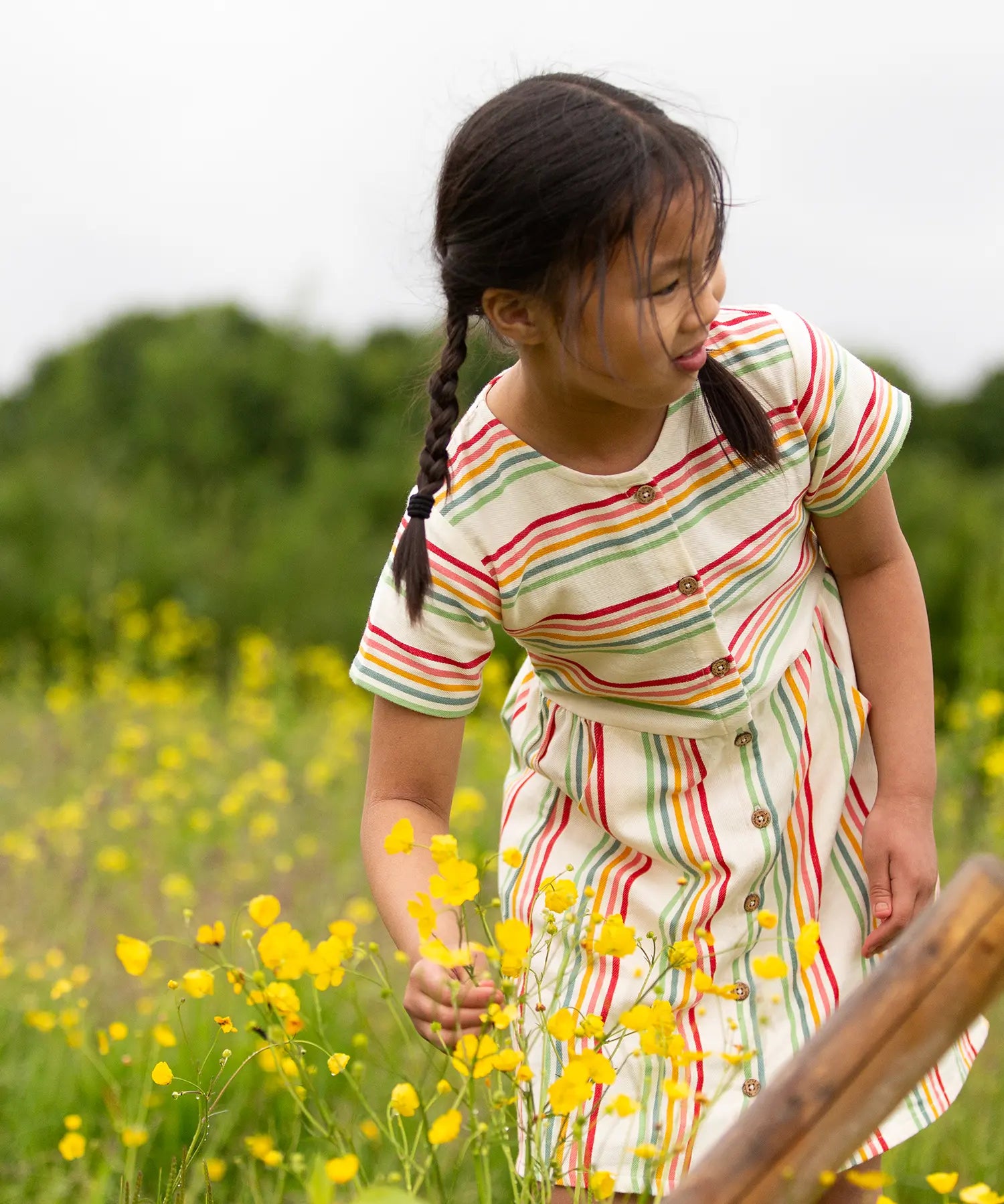 A child wearing the Little Green Radicals cream rainbow striped short sleeve button front dress.