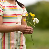 A close up of the button up front on the Little Green Radicals children's cream rainbow striped short sleeve dress being worn by a child.