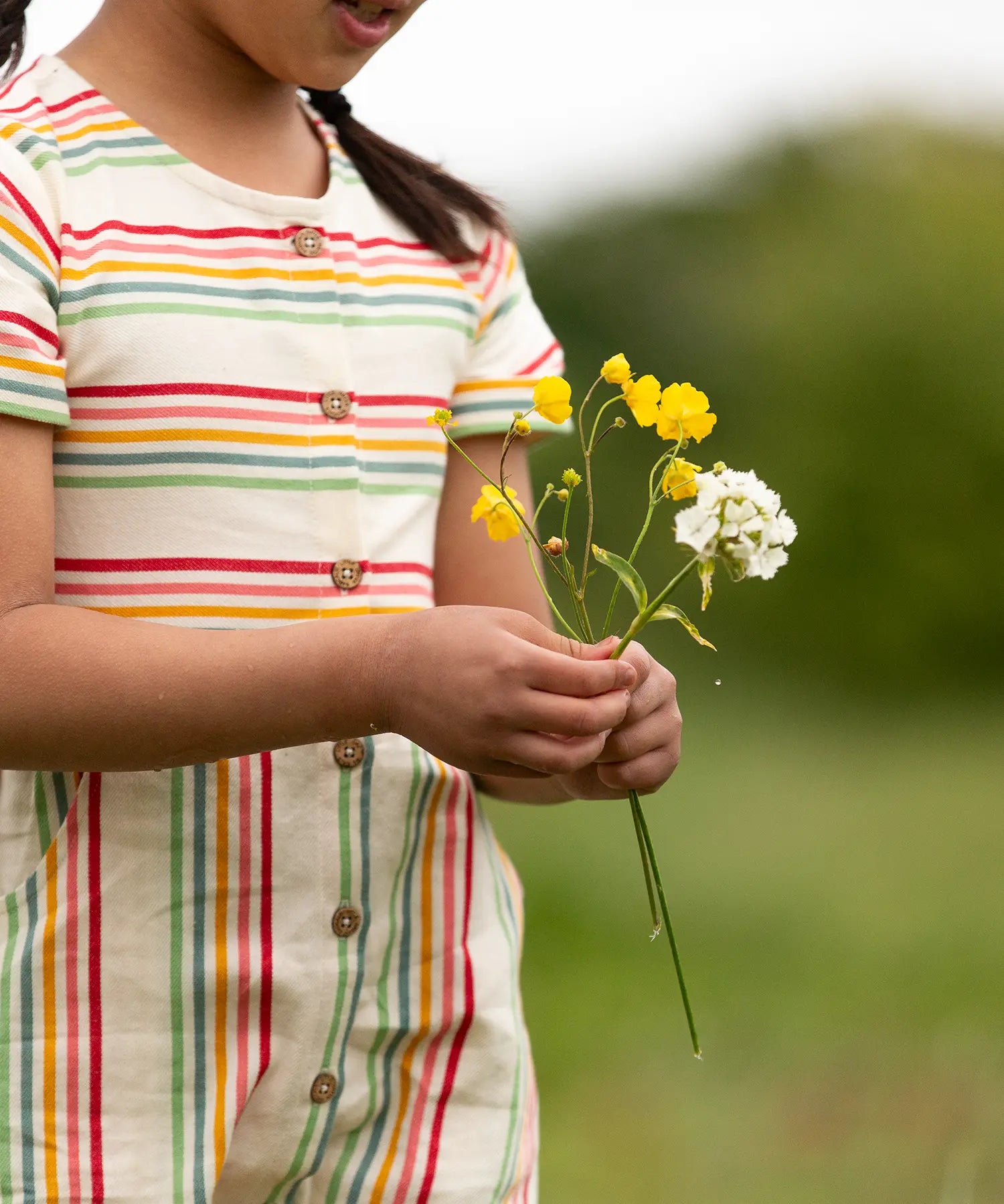 A close up of the button up front on the Little Green Radicals children's cream rainbow striped short sleeve dress being worn by a child.