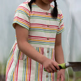 A close up of the button up front and side pockets on the Little Green Radicals children's cream rainbow striped short sleeve dress being worn by a child.