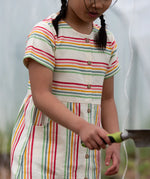 A close up of the button up front and side pockets on the Little Green Radicals children's cream rainbow striped short sleeve dress being worn by a child.