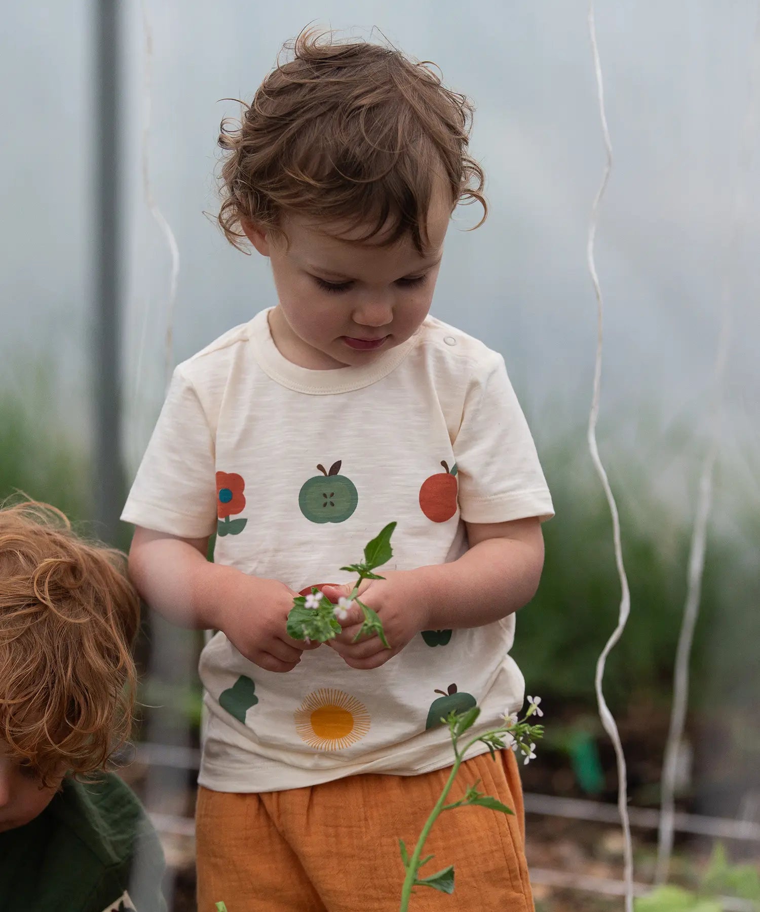 Close up of the nature illustrations on the front of the Little Green Radicals cream vintage style kids organic cotton t-shirt being worn with peach shorts.