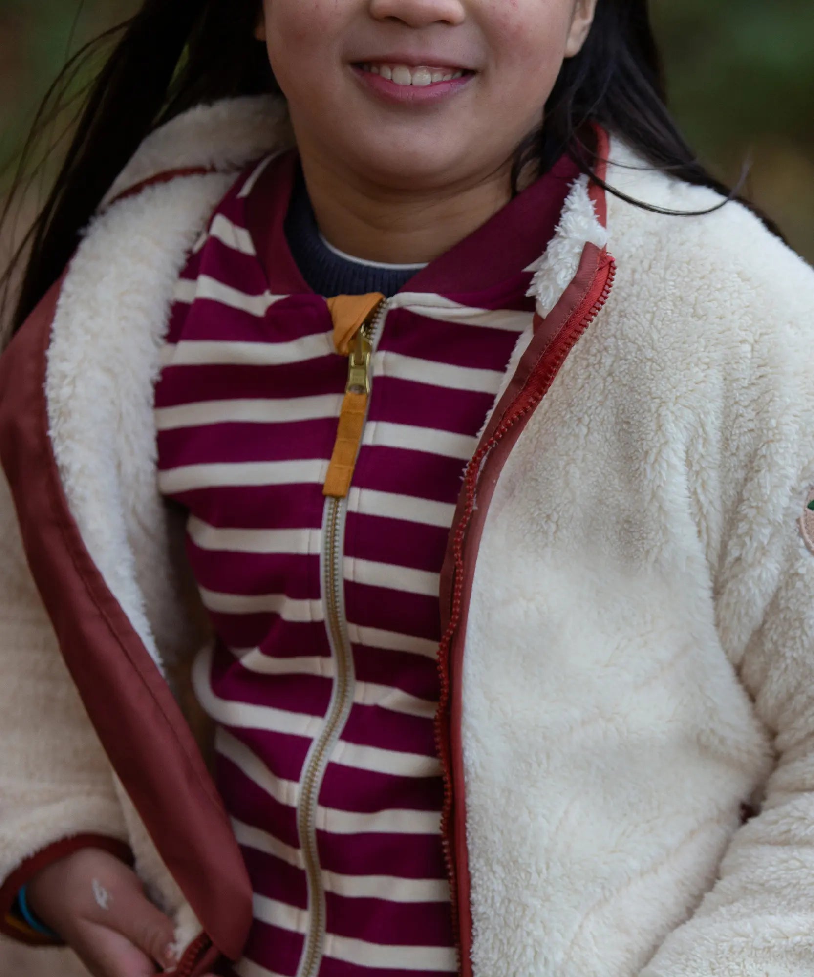 Child wearing a Little Green Radicals cream zip up cosy recycled fleece jacket with the zip open.