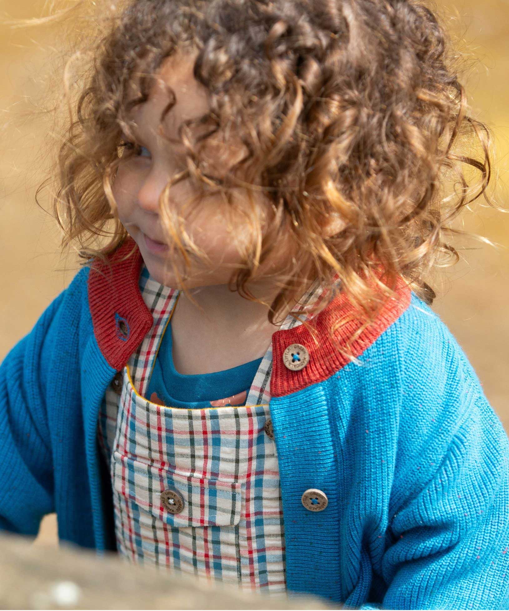 A close up of a child wearing the  Little Green Radicals From One To Another Deep Blue Colour Block Knitted Cardigan. This organic cotton cardigan is part of a wide range of organic cotton, Fairtrade children's clothing and outerwear available here at Babipur.