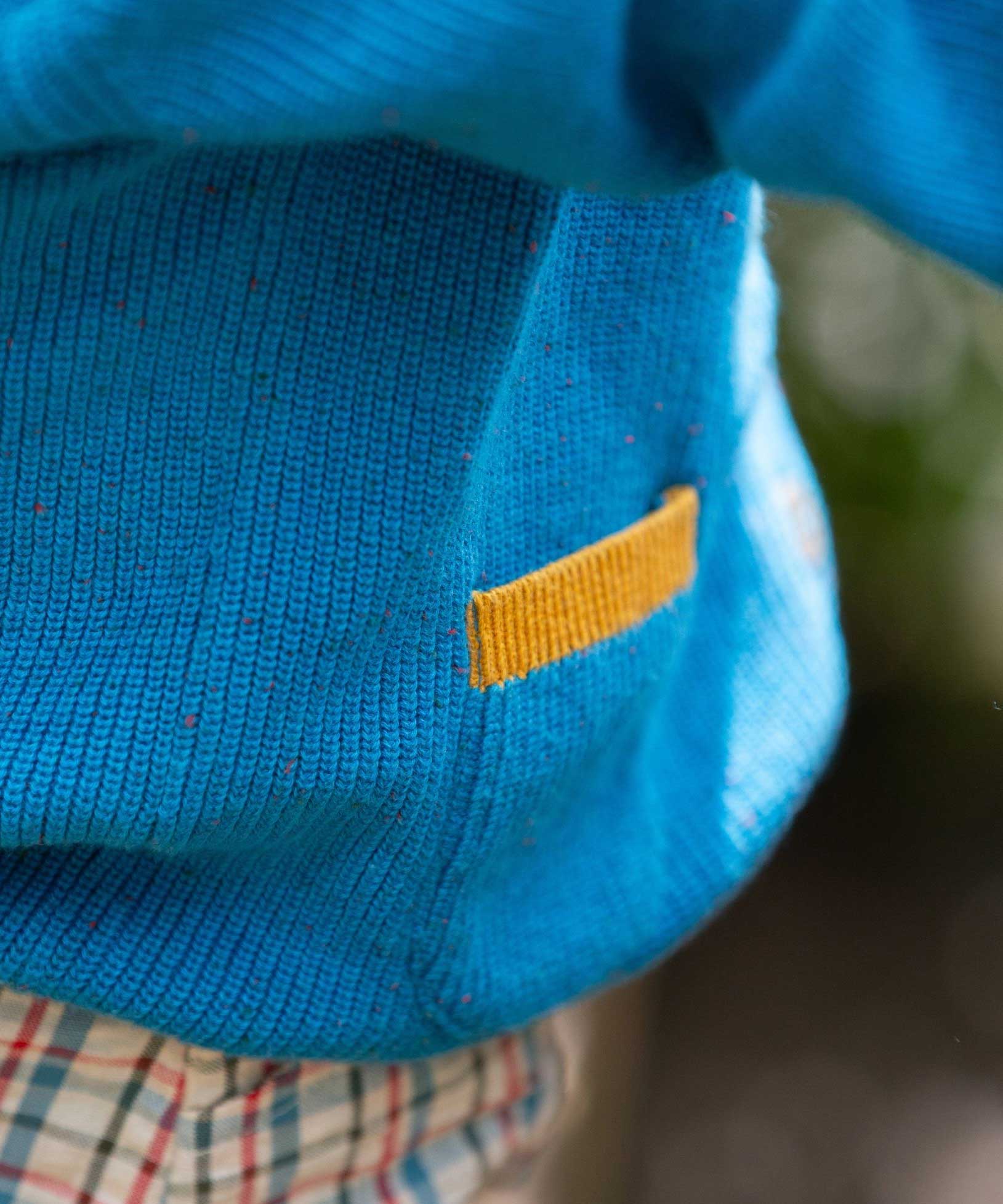 A close up of the pocket with a child wearing the Little Green Radicals From One To Another Deep Blue Colour Block Knitted Cardigan. This organic cotton cardigan is part of a wide range of organic cotton, Fairtrade children's clothing and outerwear available here at Babipur.