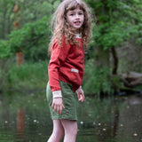A child wearing a Little Green Radicals From One To Another Burnt Ochre Pointelle Knitted Cardigan with green coloured shorts. Little green Radicals have a wide range of organic cotton, Fairtrade children's clothing and outerwear available here at Babipur.