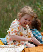 Child wearing the Little Green Radicals organic cotton short pyjamas set in cream with a pink and yellow flora print. 