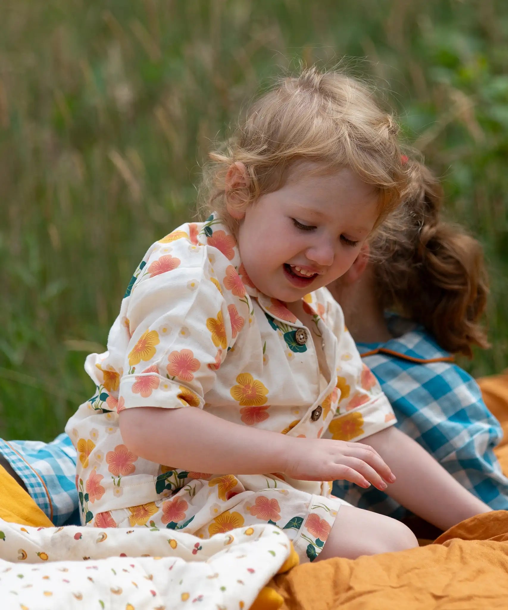 Child wearing the Little Green Radicals organic cotton short pyjamas set in cream with a pink and yellow flora print. 