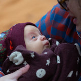 Young babywearing the Little Green Radicals folk birds knitted purple bobble hat.