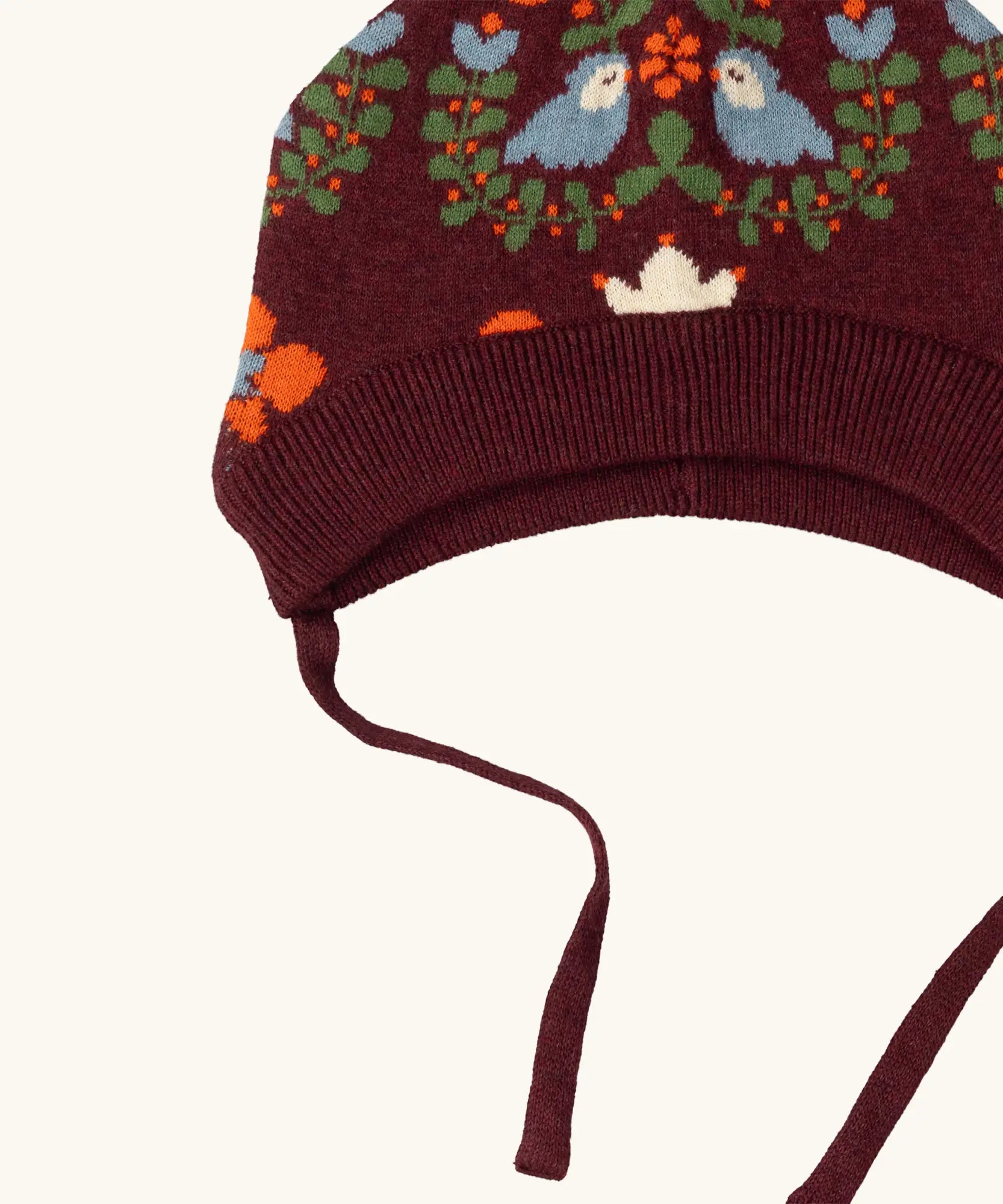 Close up showing the chin tie straps on the Little Green Radicals folk birds knitted purple bobble hat.