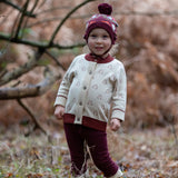 Child wearing the Little Green Radicals folk birds knitted purple bobble hat with penguin cardigan and purple joggers.