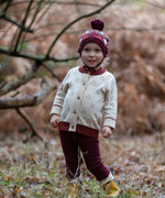 Child wearing the Little Green Radicals folk birds knitted purple bobble hat with penguin cardigan and purple joggers.