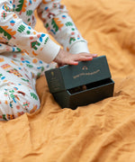 Child holding the green gift box packaging that the Little Green Radicals folk tales ankle socks 3 pack comes in.