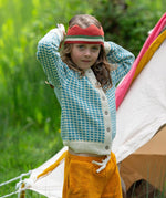 A child wearing the blue and white From One To Another Knitted Cardigan by Little Green Radicals with yellow gold coloured shorts and a knitted red crown. 