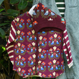 Little Green Radicals Organic Sherpa Reversible Gilet featuring the Folk Birds print with a knitted hat featuring the same print with a long sleeved striped top shown underneath.