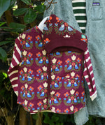 Little Green Radicals Organic Sherpa Reversible Gilet featuring the Folk Birds print with a knitted hat featuring the same print with a long sleeved striped top shown underneath.